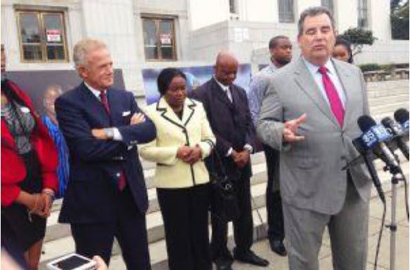 Agu family attorney gives a press conference in front of podium, the Agu family lowers their heads behind him.